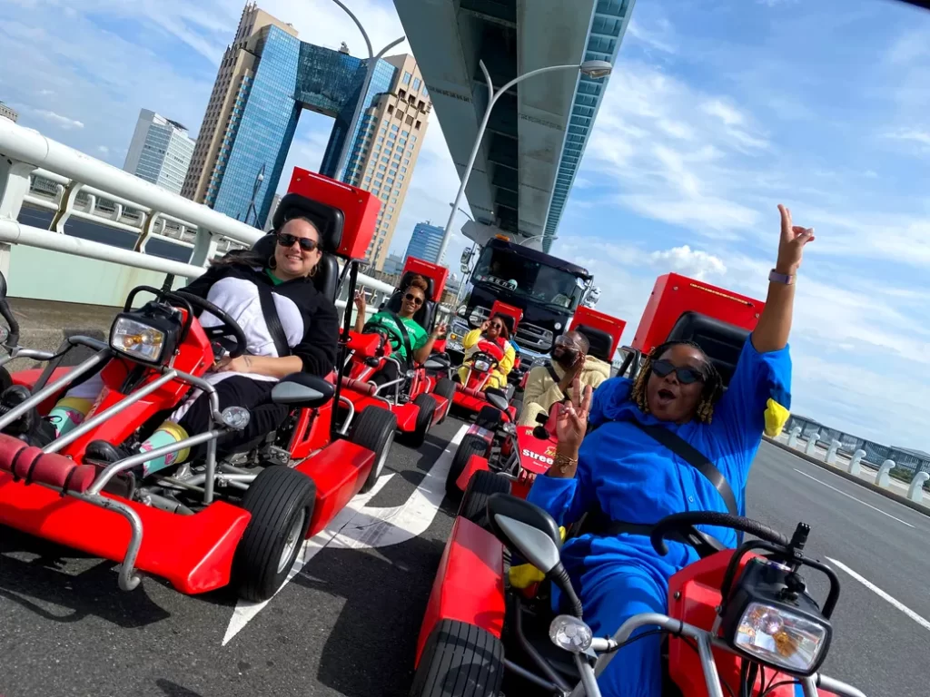 Group of people in red go-karts cruising on a city bridge, smiling with skyscrapers in the background.